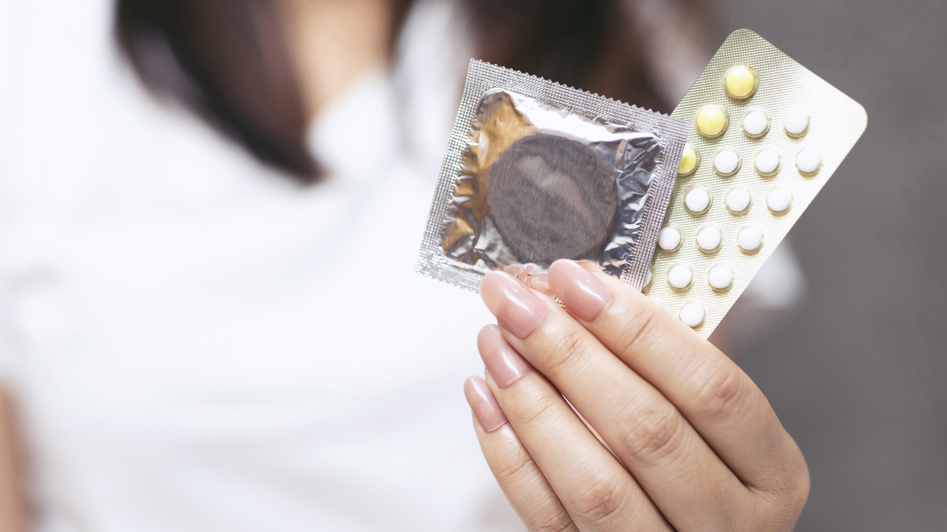 Frau hält verpacktes Kondom und Blister mit Anti-Baby-Pille in die Kamera