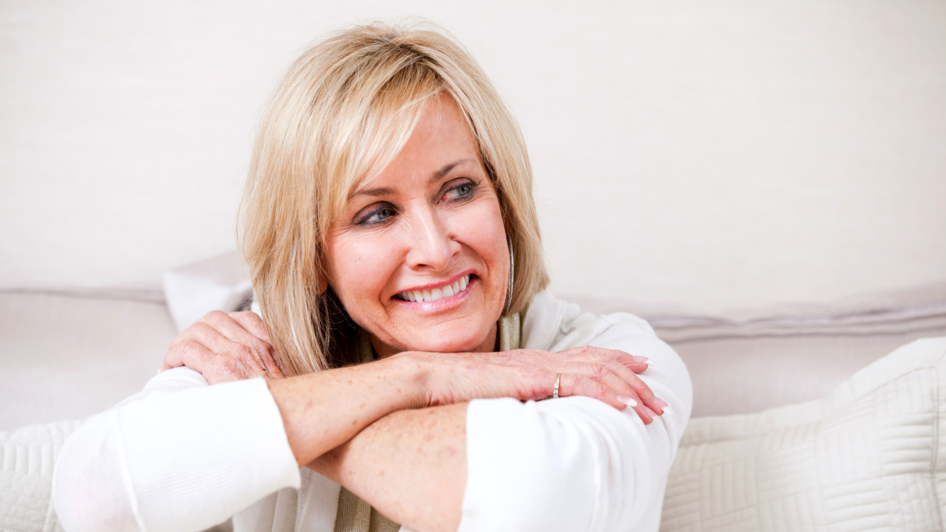 Best Ager Frau hat Hande auf die Knie gestützt und lächelt zur Seite